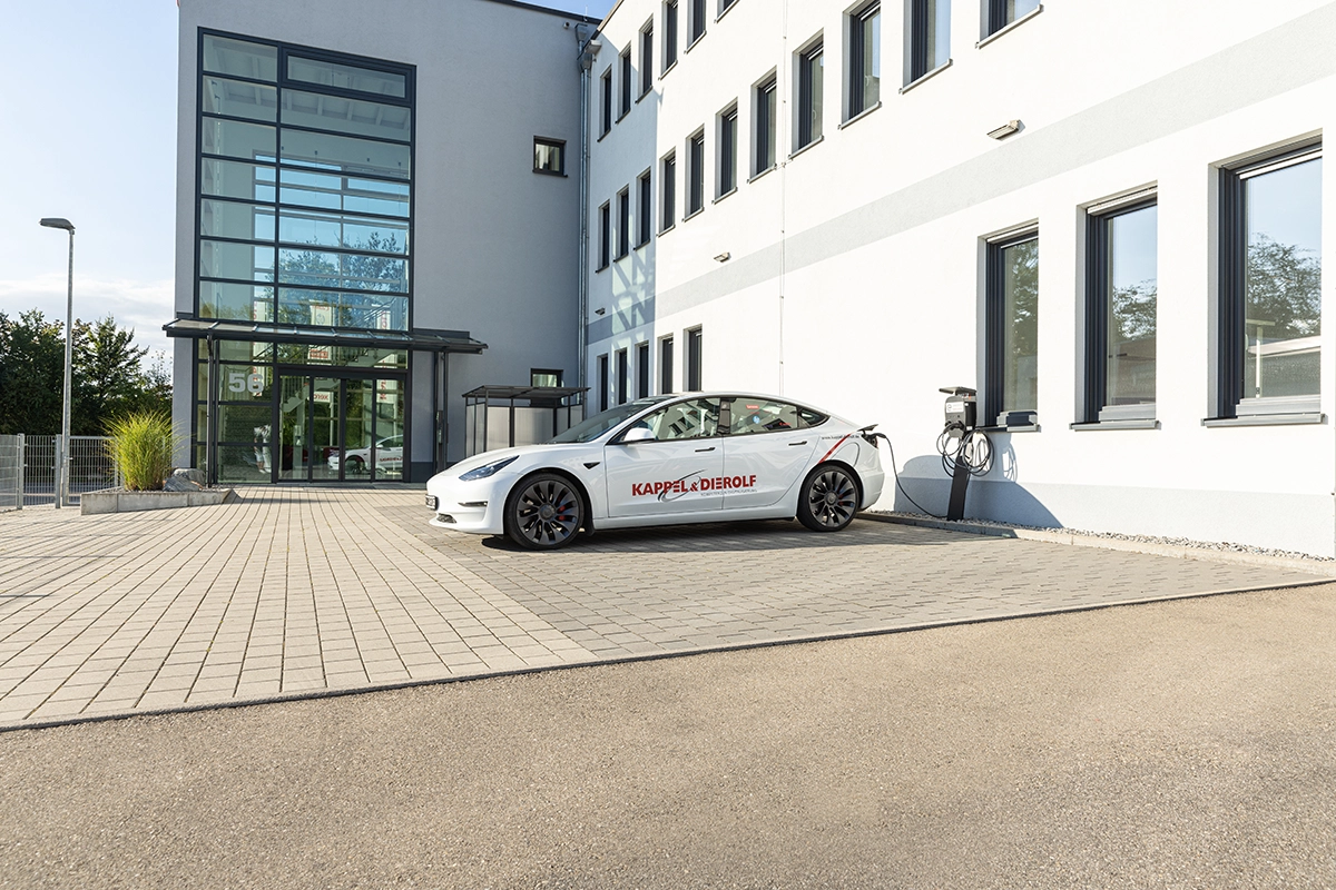 Elektroauto lädt an Ladestation vor modernem Bürogebäude auf gepflastertem Parkplatz.