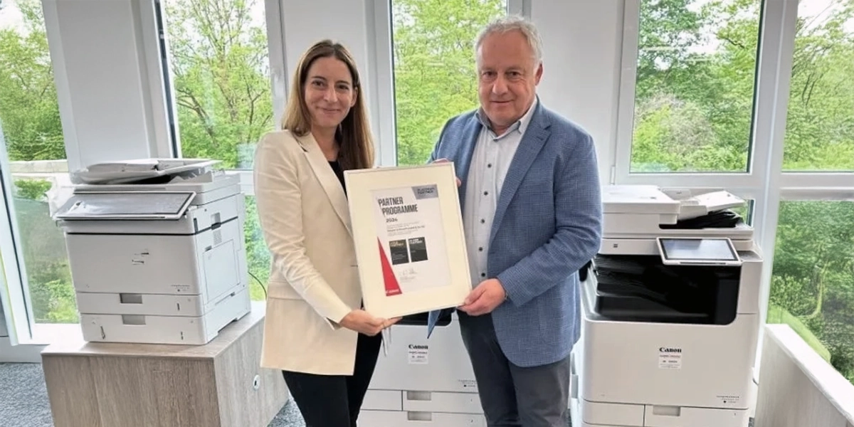 Kappel-Dierolf-Blog_Gold_Partner_2024 Zwei Personen halten eine Urkunde in einem Büro mit zwei Druckern im Hintergrund.