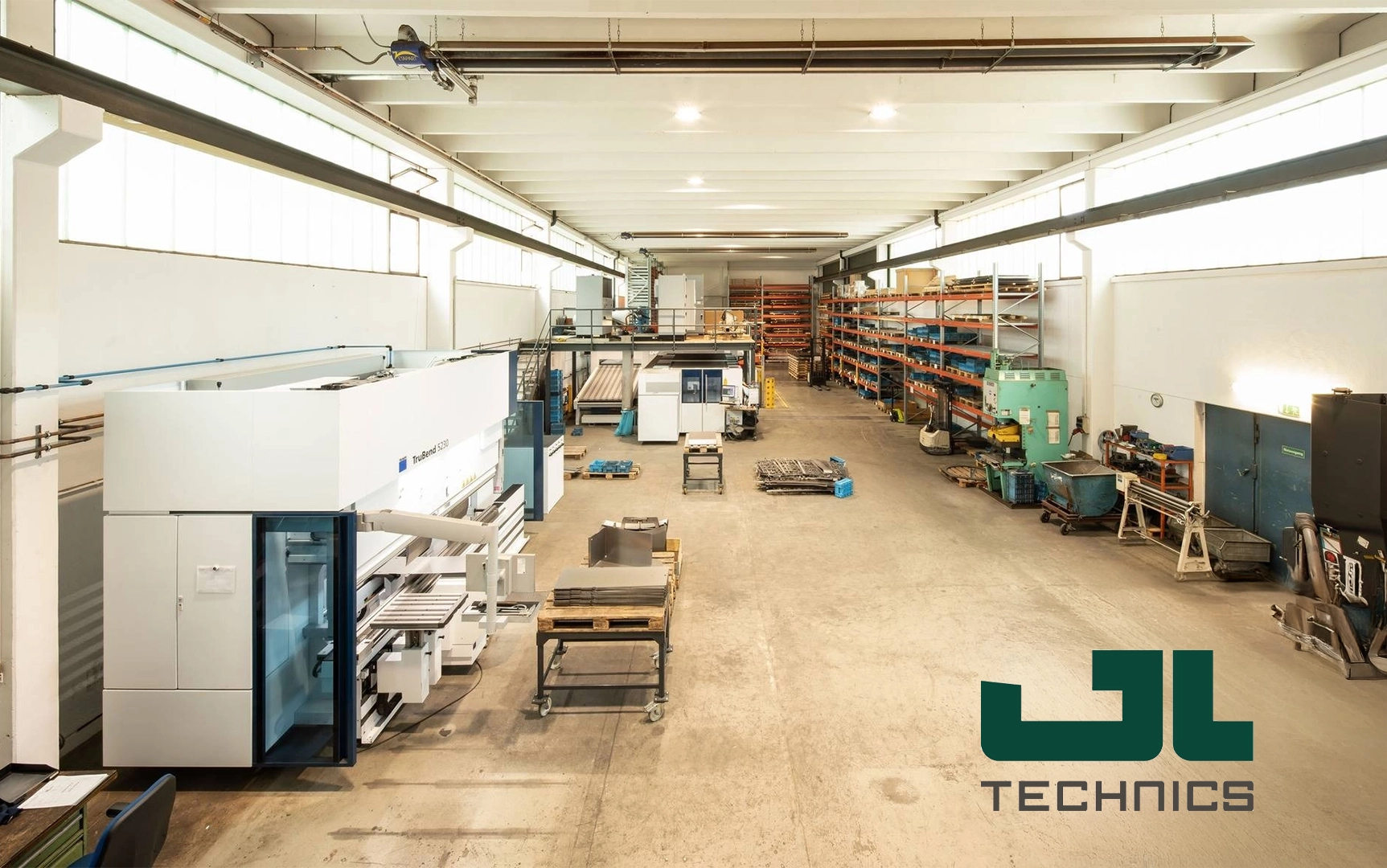 Große, helle Werkshalle mit Maschinen, Regalen und Materialien. Logo „JL Technics“ im Vordergrund.