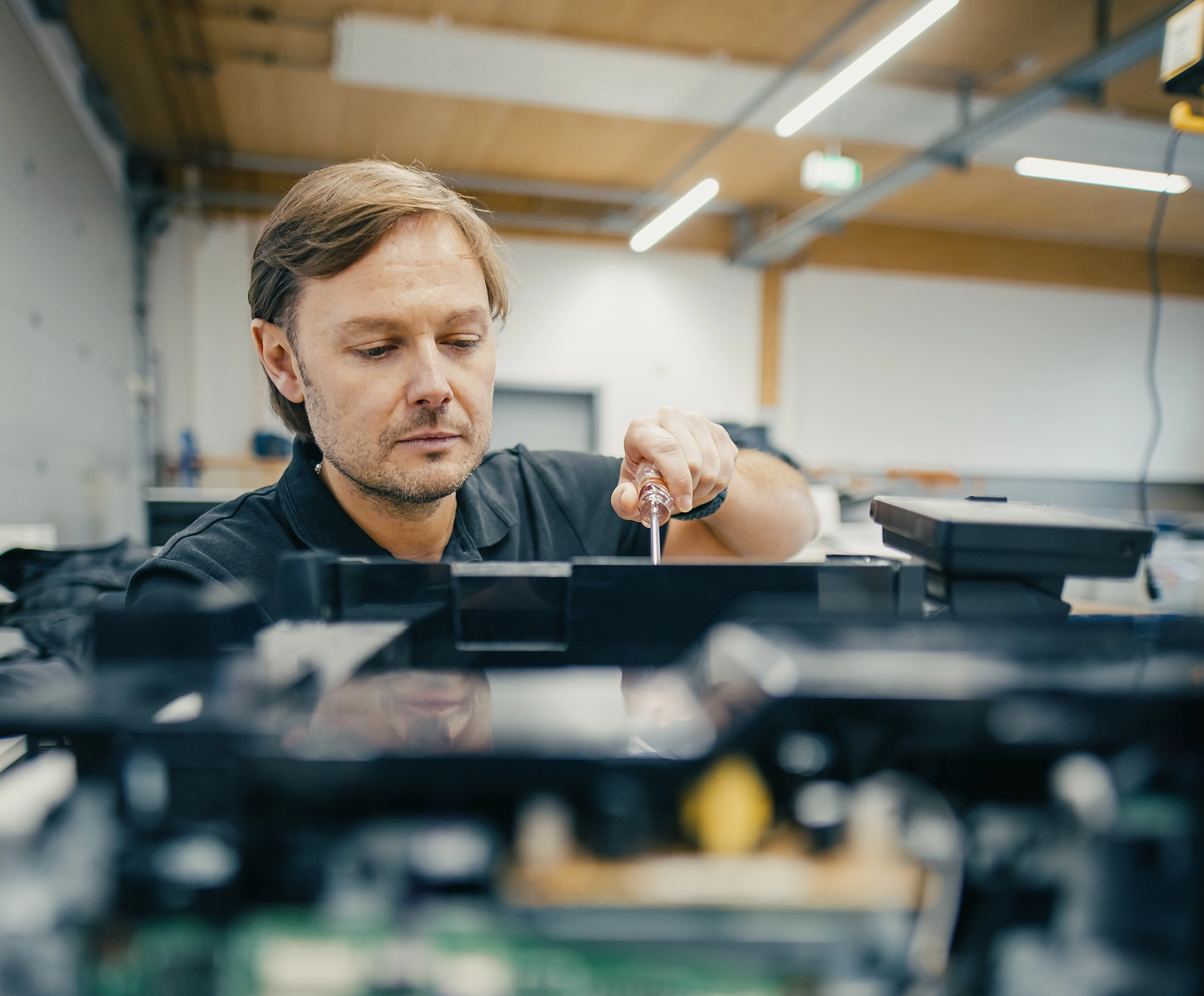 Ein Mann arbeitet konzentriert mit einem Schraubenzieher an einem elektronischen Gerät in einer Werkstatt.