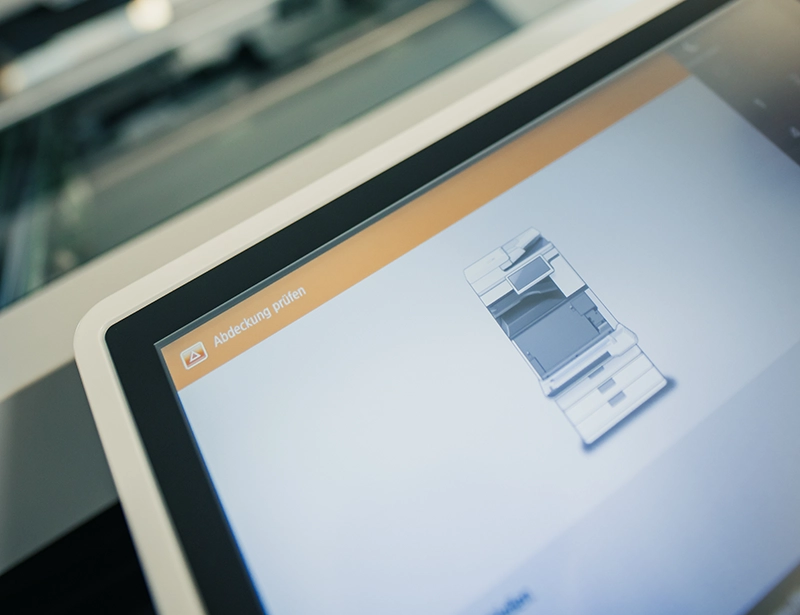 Nahaufnahme des Touchscreens eines Druckers, zeigt Diagramm und Text Abdeckung prüfen zur Fehlerbehebung.