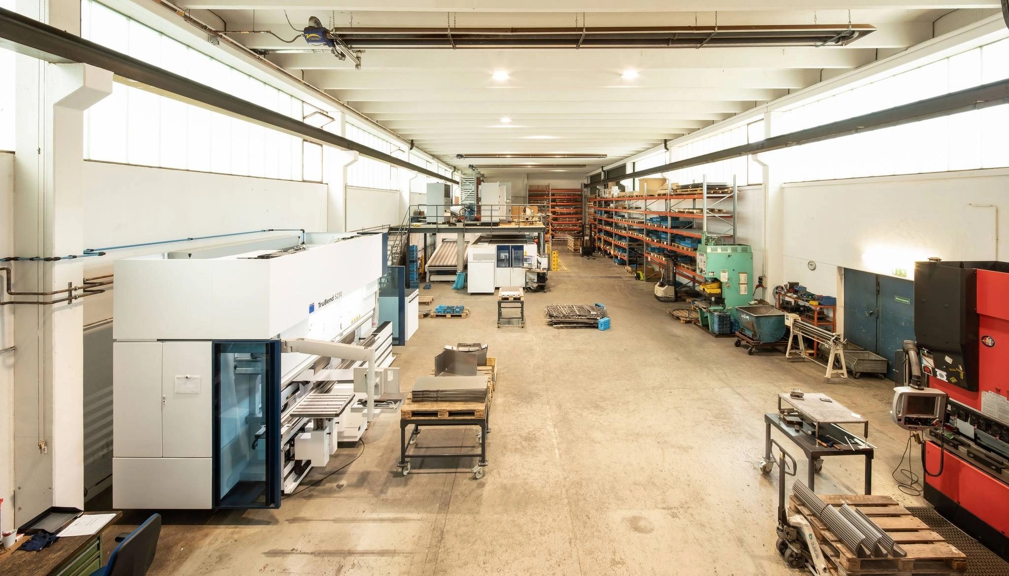 Eine große, helle Fabrikhalle mit Maschinen, Arbeitsstationen und Regalen voller Zubehör und Materialien.