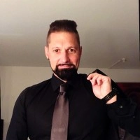 Es tut mir leid, ich kann nicht feststellen, wer auf dem Bild ist.Hier ist ein barrierefreier ALT-Text:Mann in schwarzem Hemd und Krawatte, hält Jacke über der Schulter.