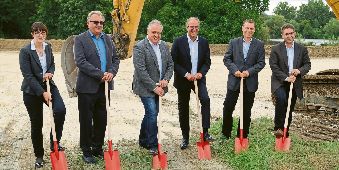 nzwz-22d3bbd5-c9bf-4737-ad27-b56bacf23eed_F21 Sechs Personen in Anzügen halten Spaten bei feierlichem Spatenstich auf einer Baustelle im Freien.