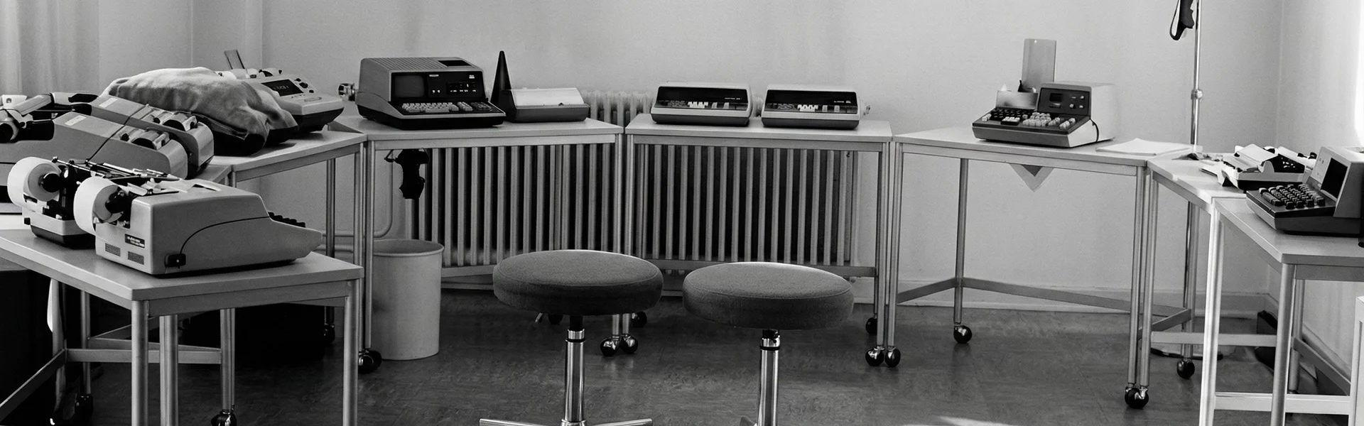 Kappel_Dierolf_Historie Schwarz-Weiß-Büro mit Schreibmaschinen und Rechenmaschinen auf Tischen, zwei gepolsterte Hocker im Vordergrund.