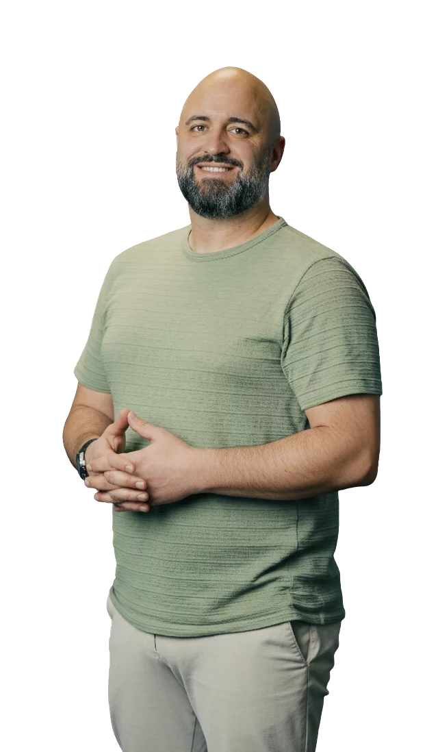 Ein Mann mit Bart in einem grünen T-Shirt steht lächelnd mit verschränkten Händen vor einem neutralen Hintergrund.