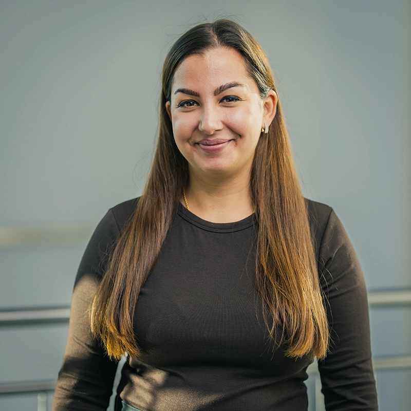 Eine lächelnde Person in schwarzem Oberteil vor neutralem grauem Hintergrund.