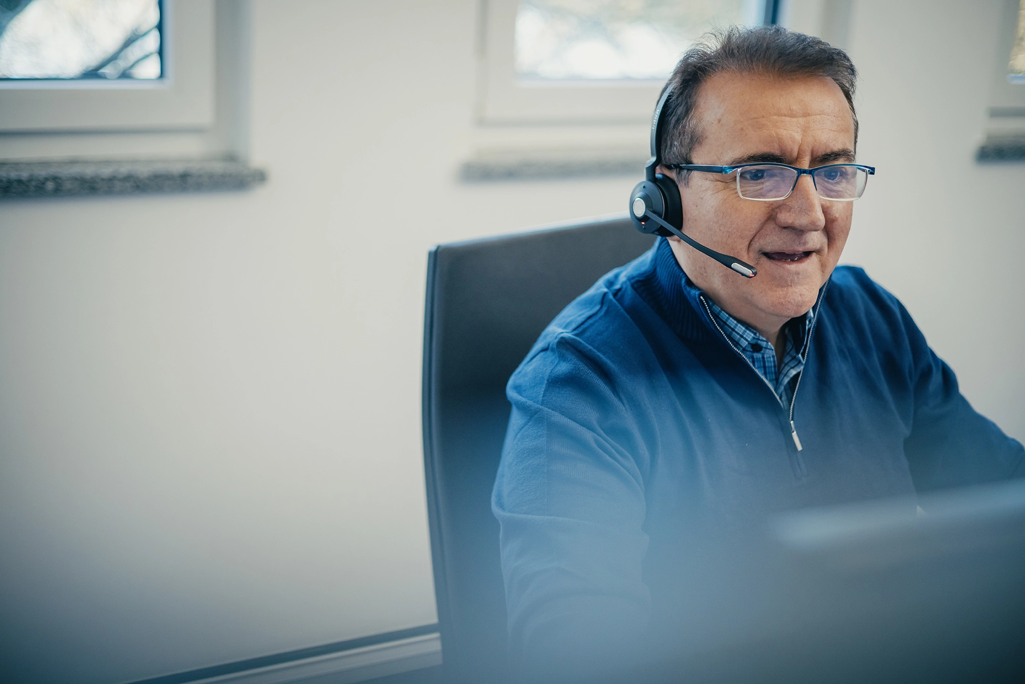 Mann mit Headset arbeitet am Computer und spricht, vermutlich in einem Büro.