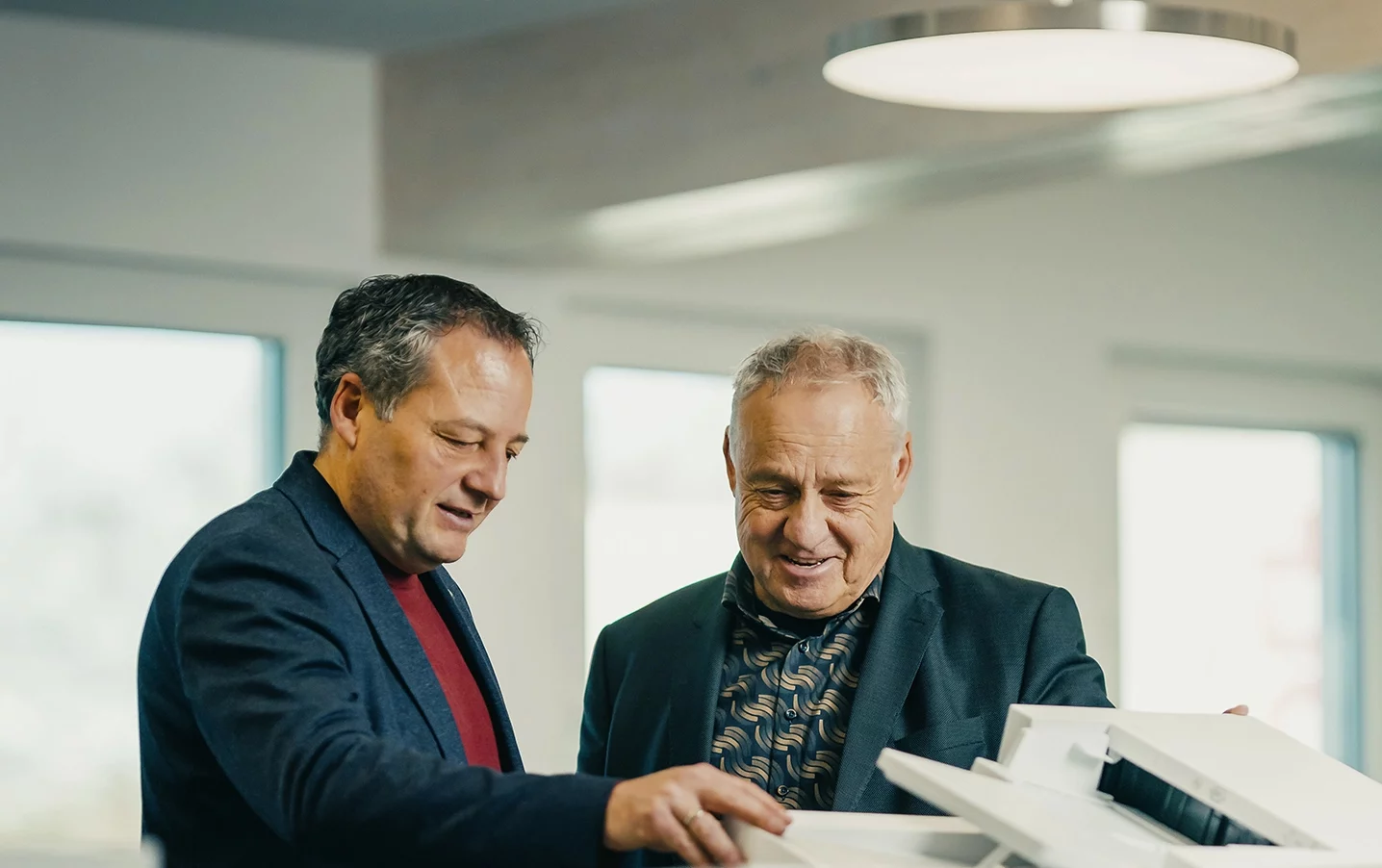 Zwei Männer stehen an einem Tisch und betrachten gemeinsam Dokumente in einem modernen Arbeitsumfeld.